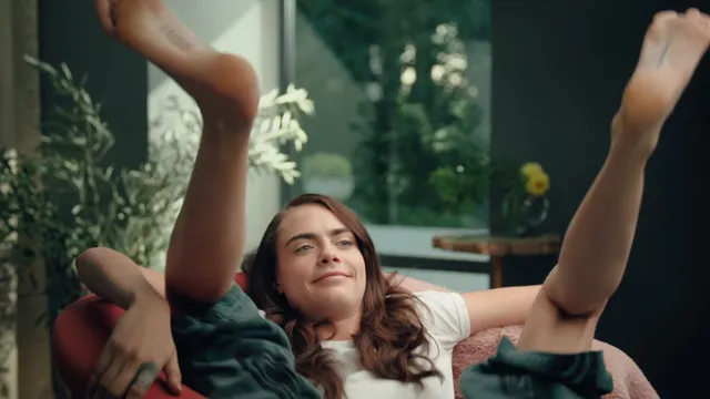 Cara Delevingne reclining outdoors with one leg raised.