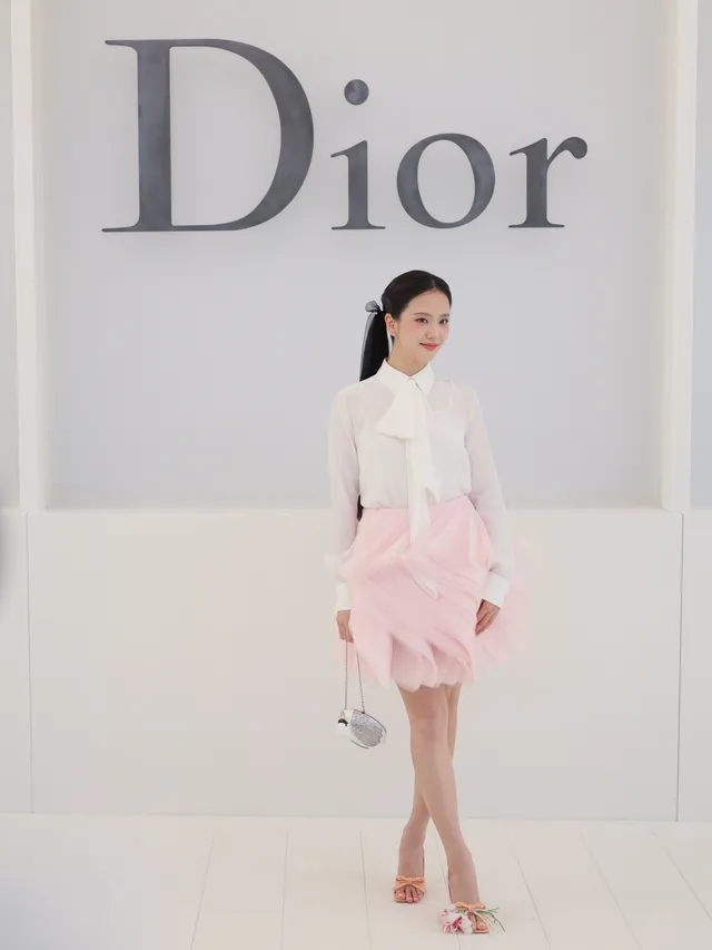 Jisoo wearing pale embellished heels with a pink skirt against a fashion-event backdrop.