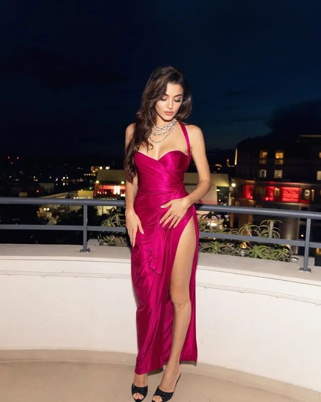 Hande Erçel posing in a pink gown and black heels on a balcony at night.