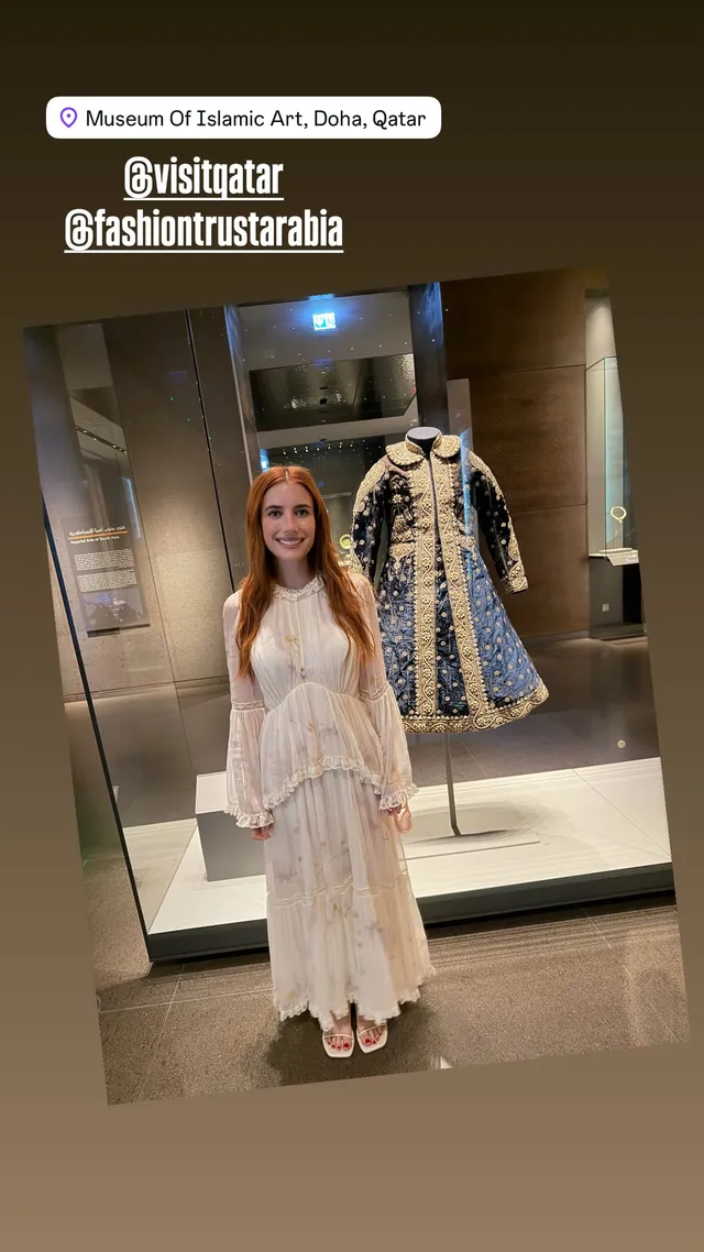 Emma Roberts posing in a cream dress in an ornate interior.