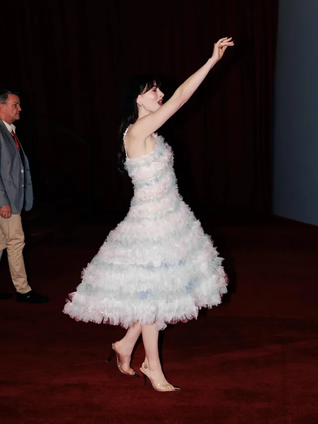 Anne Hathaway dancing barefoot in a pale feathered dress.