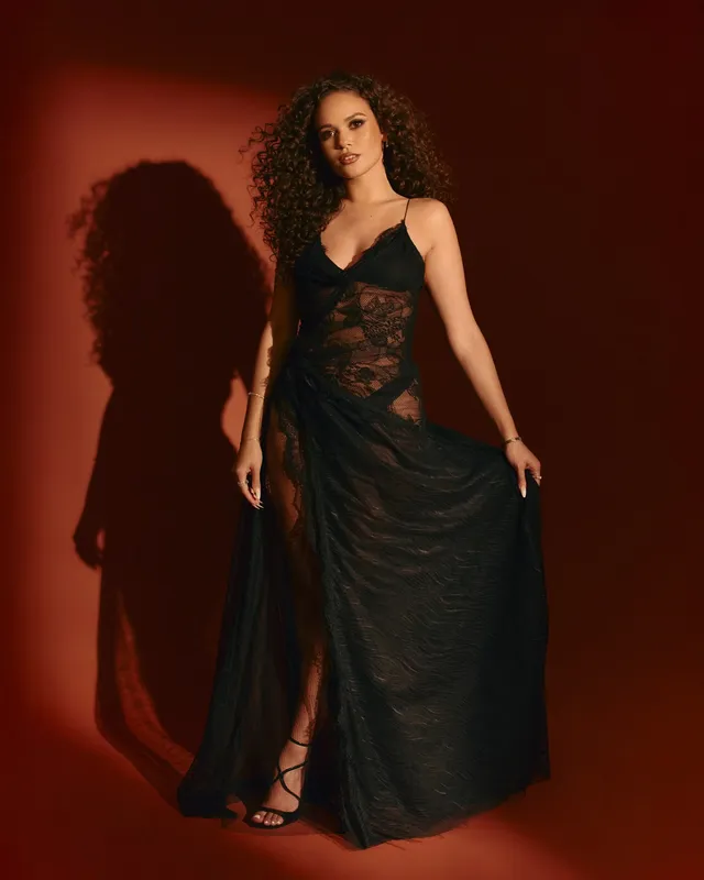 Madison Pettis wearing a long black lace dress and lace-up heels for a studio portrait.