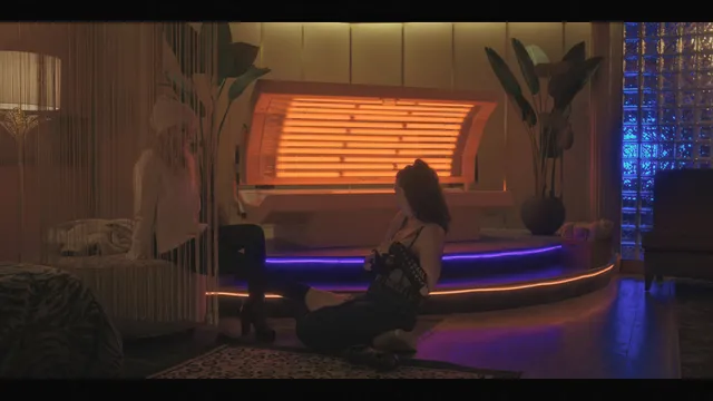 Kate Beckinsale sitting indoors with bare legs extended in a screen image.