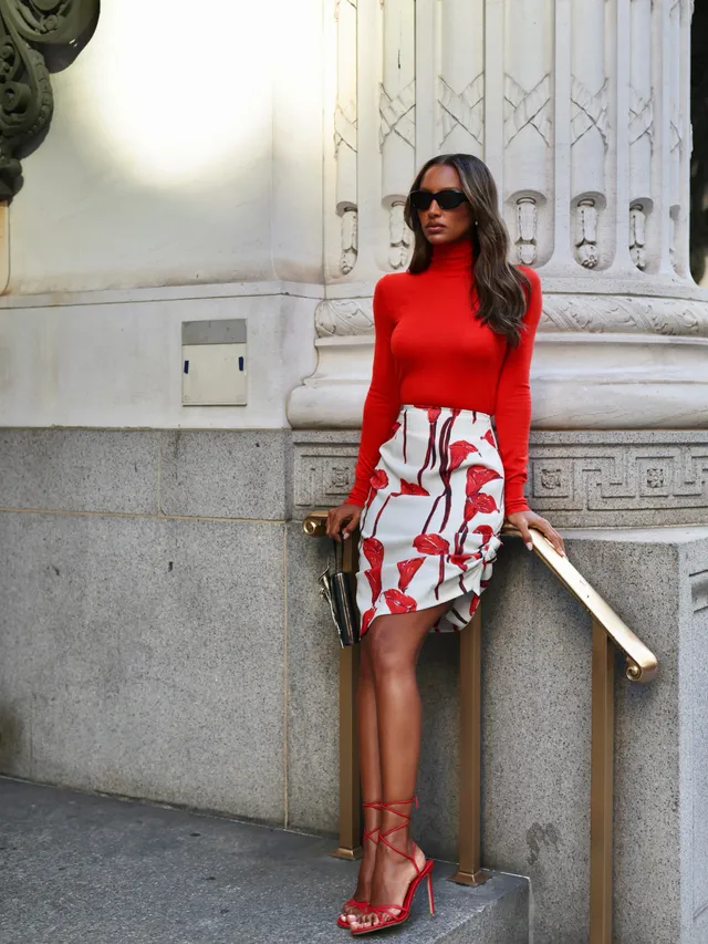 Jasmine Tookes wearing red heels with a red top and patterned skirt beside stone steps.