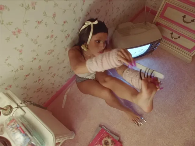 Doja Cat sitting on a bed while holding a telephone with a bare sole visible.