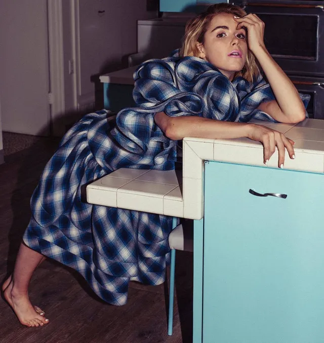 Kiernan Shipka leaning barefoot on a kitchen counter in a patterned dress.