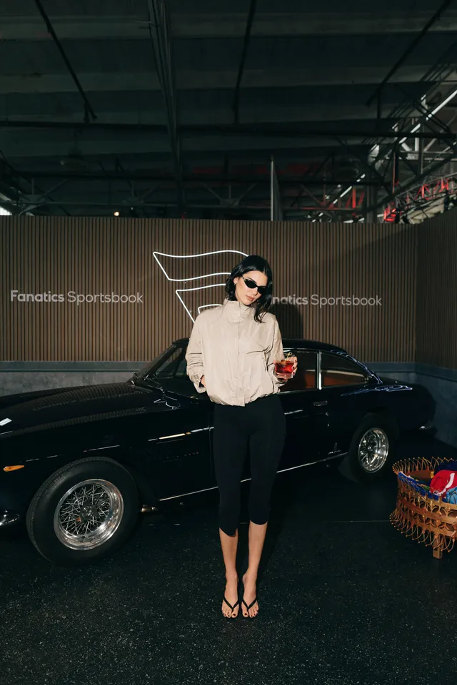 Kendall Jenner standing in black heels beside a parked car.