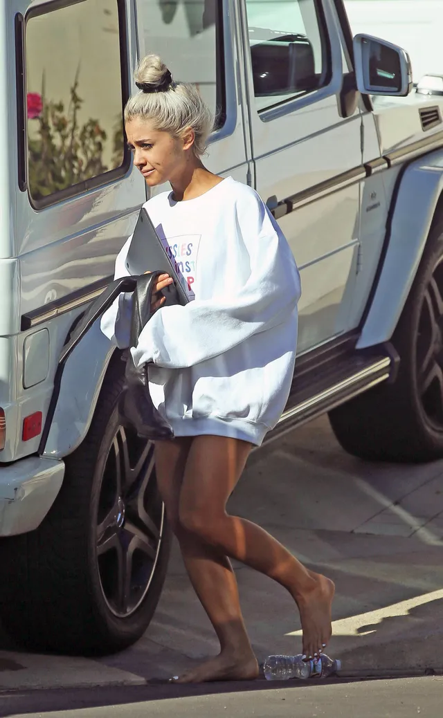 Ariana Grande walking beside a vehicle in an oversized sweatshirt.