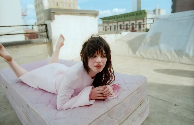 Sophie Thatcher lying barefoot on a rooftop mattress during a photo shoot.