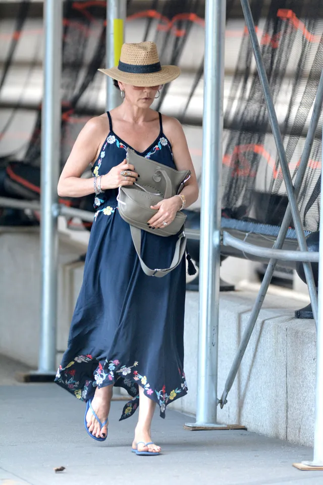 Catherine Zeta-Jones walking outdoors in a blue dress, straw hat and flip-flops.