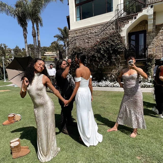 Samantha Logan standing barefoot with guests on a lawn in a long pale dress.