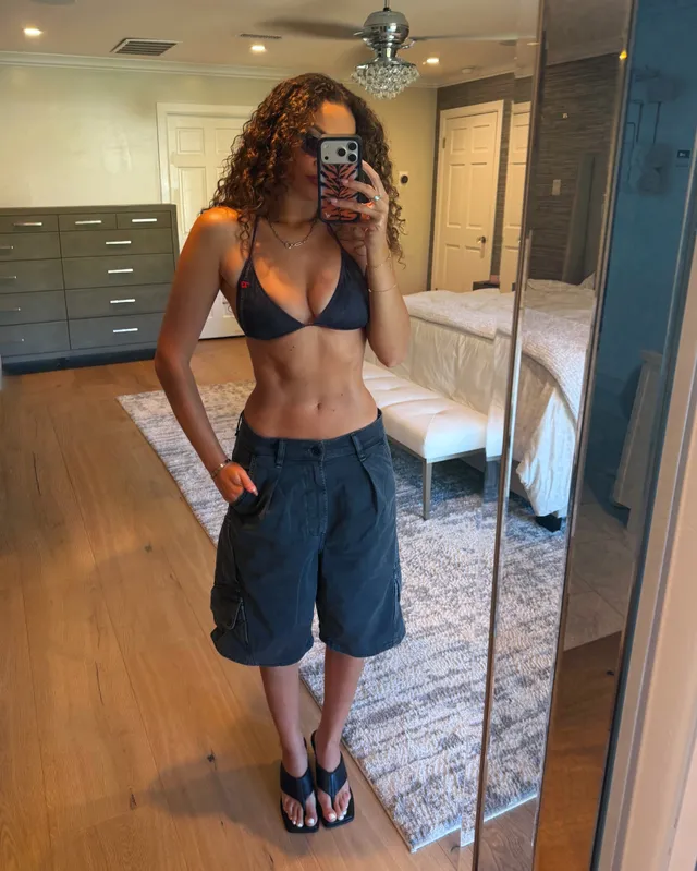 Madison Pettis taking a mirror selfie in shorts, a dark bikini top and flat sandals.