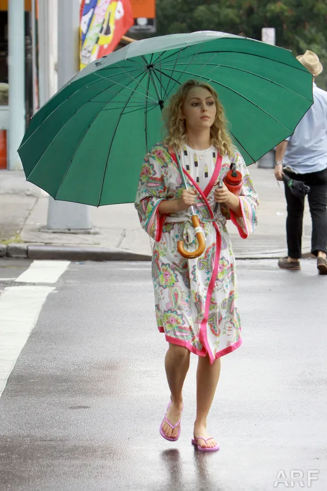 AnnaSophia Robb standing beneath a green umbrella in a patterned robe.
