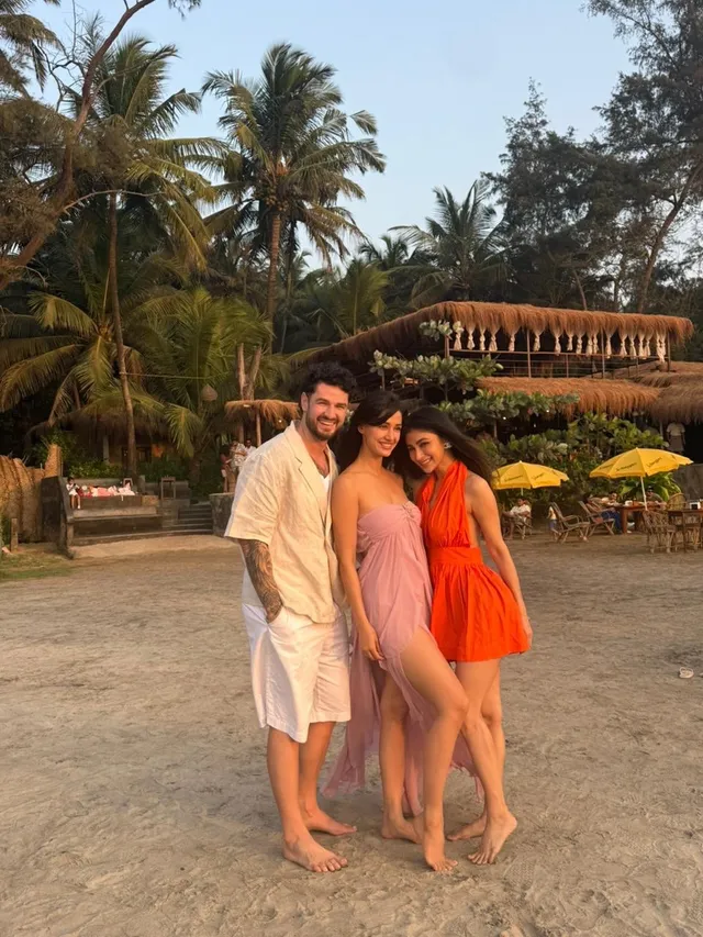 Disha Patani standing barefoot beside companions on a beach.