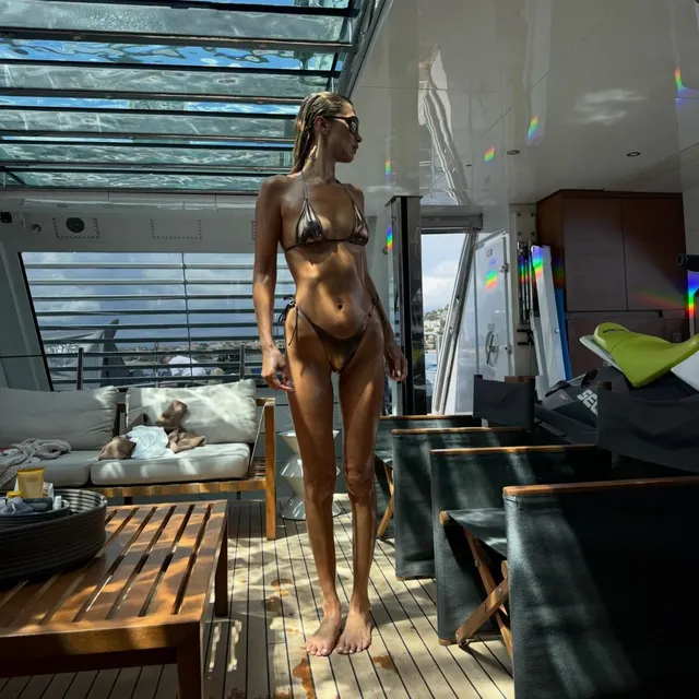 Bella Hadid standing barefoot on a boat deck.