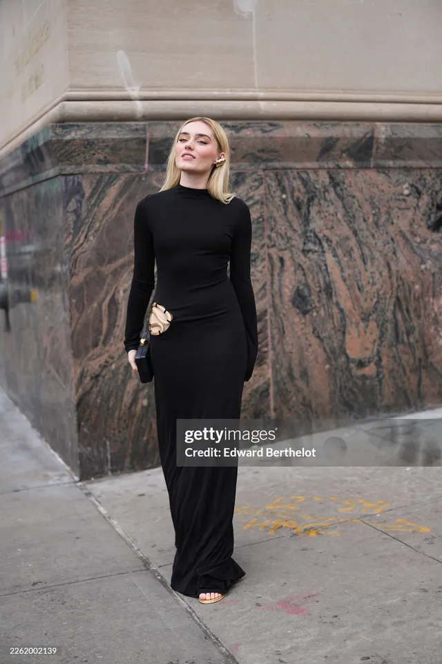 Meg Donnelly posing outside a building in a long black outfit and flat sandals.