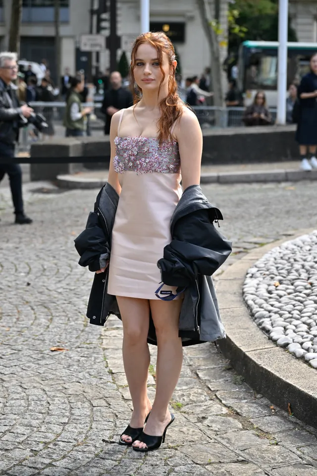 Joey King walking outside in a patterned dress and black heels.