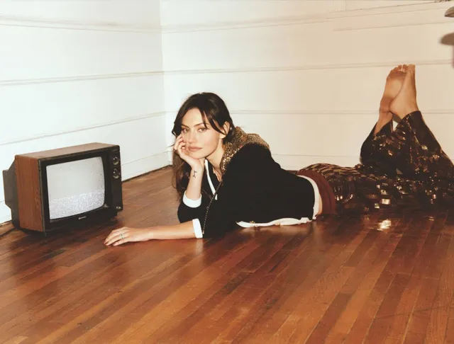 Phoebe Tonkin lying on a wooden floor beside a television.