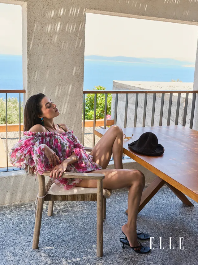 Hande Erçel sitting on a terrace in a floral dress and dark heels.