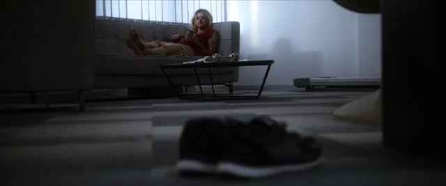 Samara Weaving reclining with a bare sole visible in a dimly lit film scene.