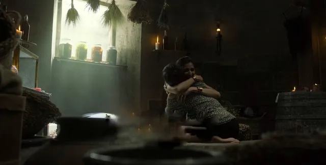 Úrsula Corberó sitting barefoot with a man in a dimly lit room in a scene.