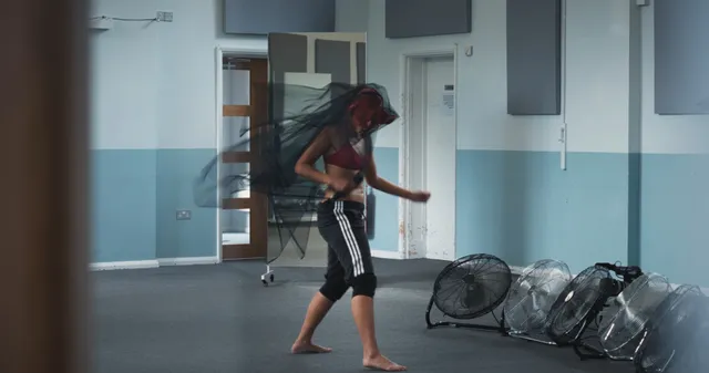 Naomi Scott standing barefoot beside floor fans in a rehearsal room.