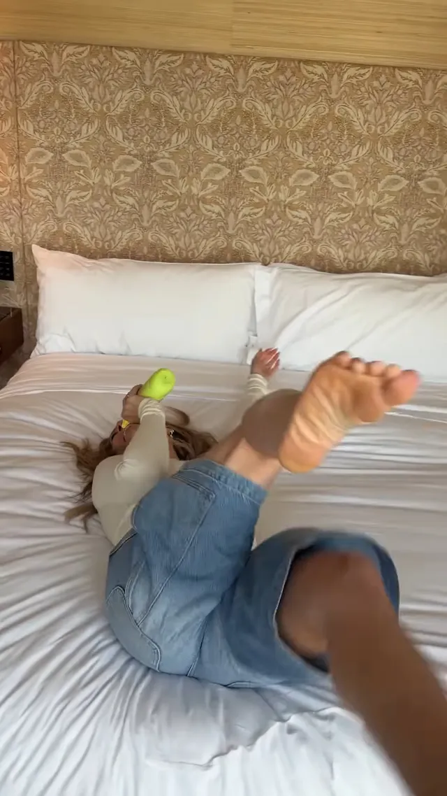 Hilary Duff lying on a bed in denim shorts with one bare sole raised.