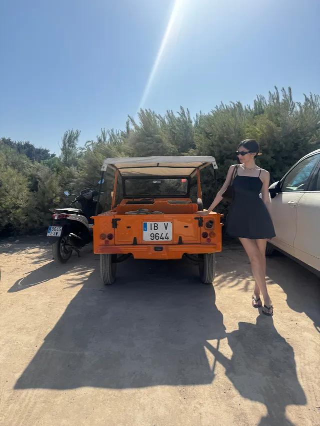 Gemma Chan standing beside an orange vehicle in flat sandals.