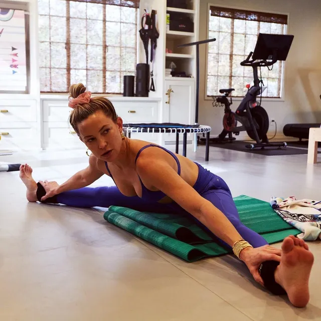 Kate Hudson stretching on a yoga mat with her legs extended.