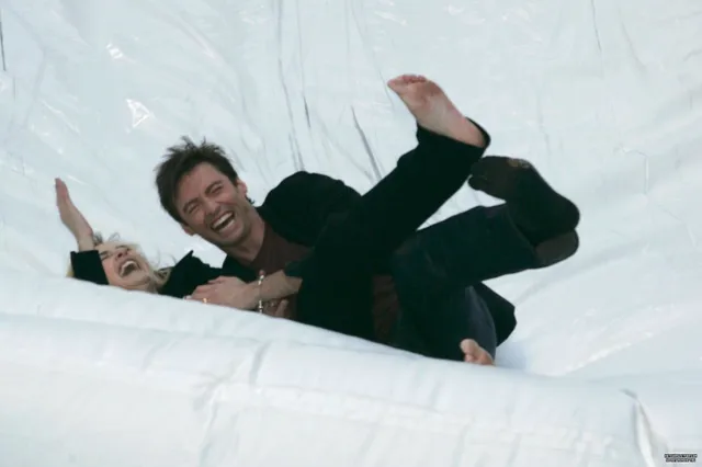 Kate Winslet reclining barefoot beside a companion on a white background.