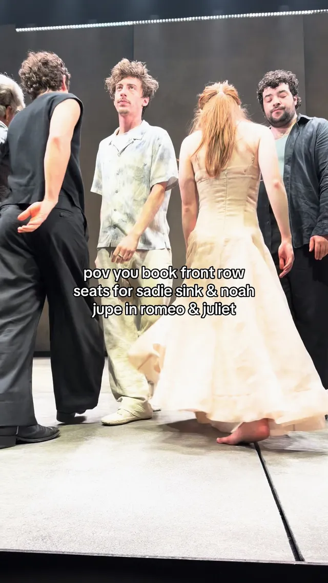 Sadie Sink standing barefoot beside actors on a theatre stage.