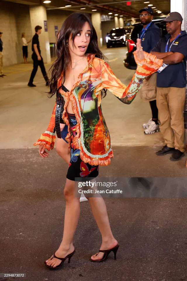 Camila Cabello gesturing in a colorful outfit and black heels.
