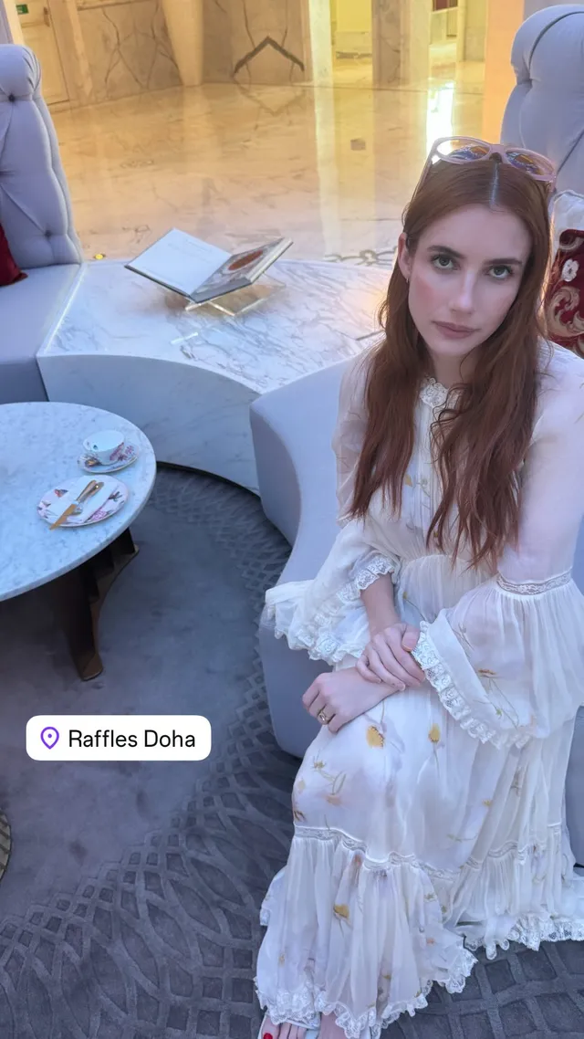 Emma Roberts sitting in a white dress beside a table.
