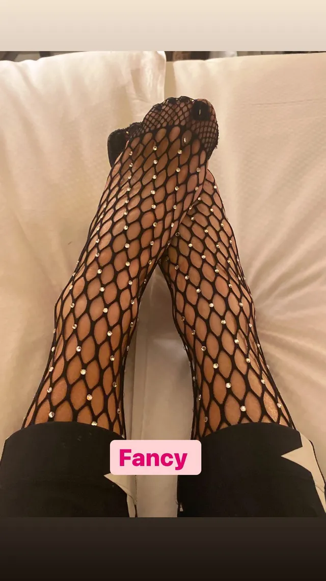 Kate Beckinsale resting crossed legs on pale bedding in patterned tights.