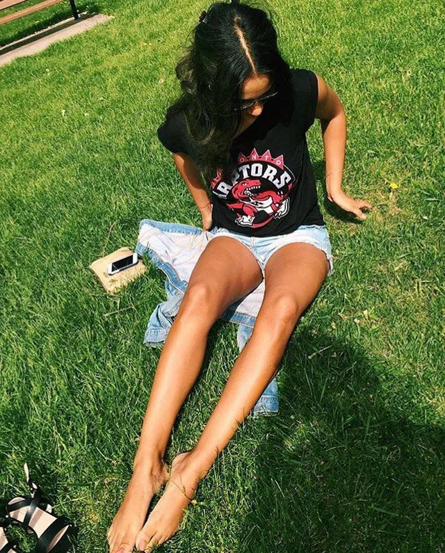 Greta Onieogou sitting barefoot on grass in denim shorts and a dark T-shirt.