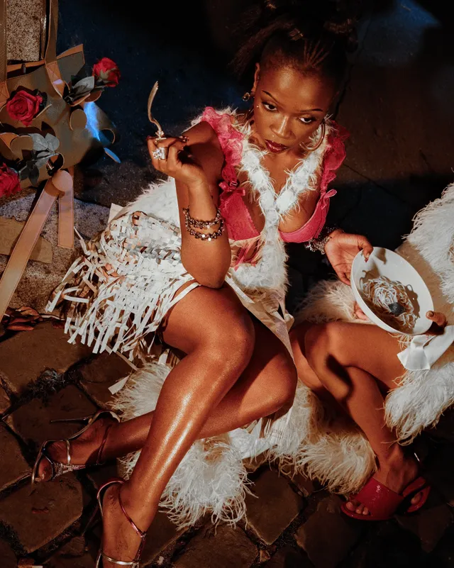 Adèle Exarchopoulos sitting with a guest in feathered outfits and sandals.