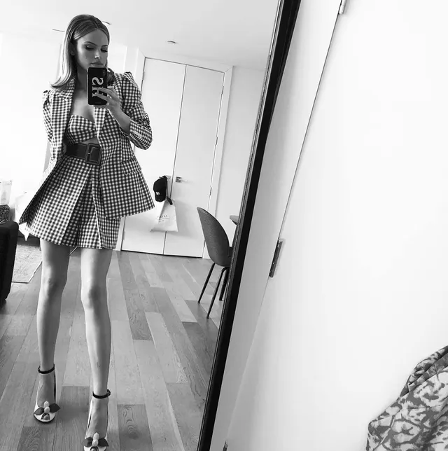 Halston Sage taking a mirror selfie in a checked skirt set and metallic heels.