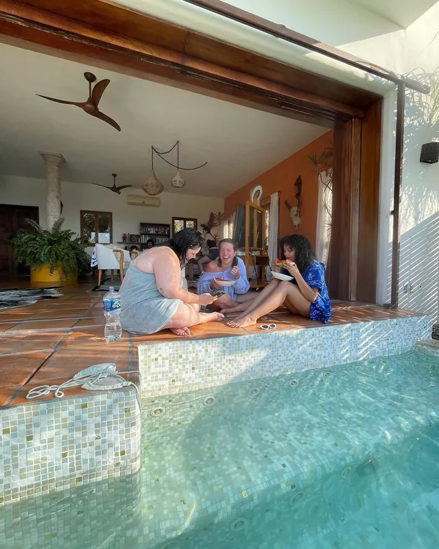 Whitney Peak sitting barefoot with friends beside a swimming pool.