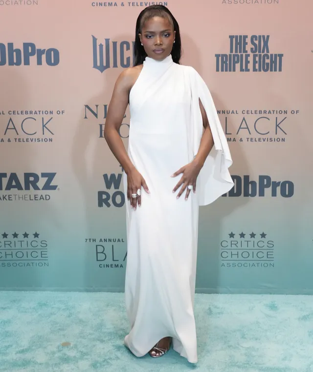Ryan Destiny posing in a white gown and metallic heels on a carpet.