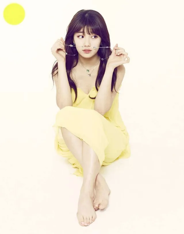 Bae Suzy sitting barefoot in a yellow dress.