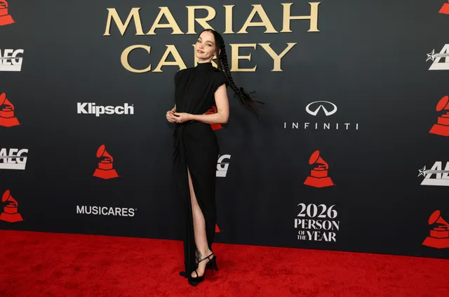 Dove Cameron wearing a long black gown and heels at a music event.
