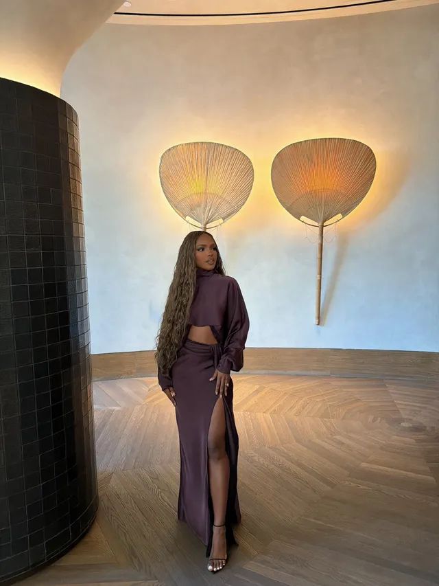 Ryan Destiny standing in a purple skirt set and metallic heels indoors.
