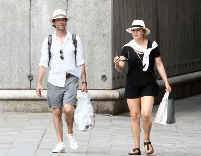 Kate Winslet walking outdoors in a black outfit and sandals beside a companion.