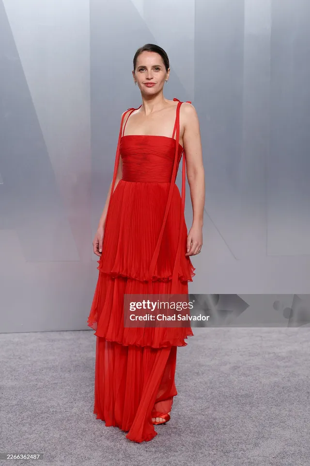 Felicity Jones posing in a flowing red dress at an event.