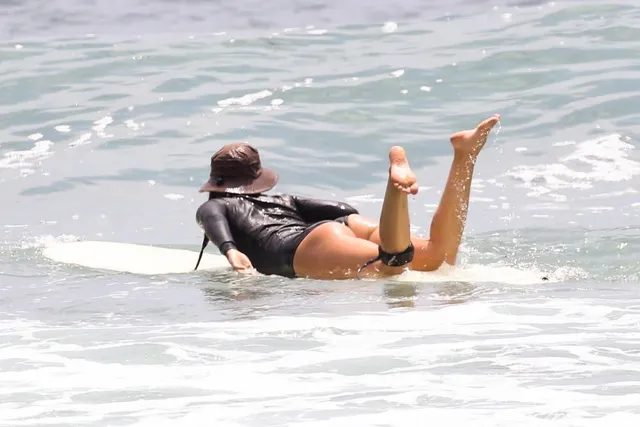 Leighton Meester lying on a surfboard in shallow sea water.