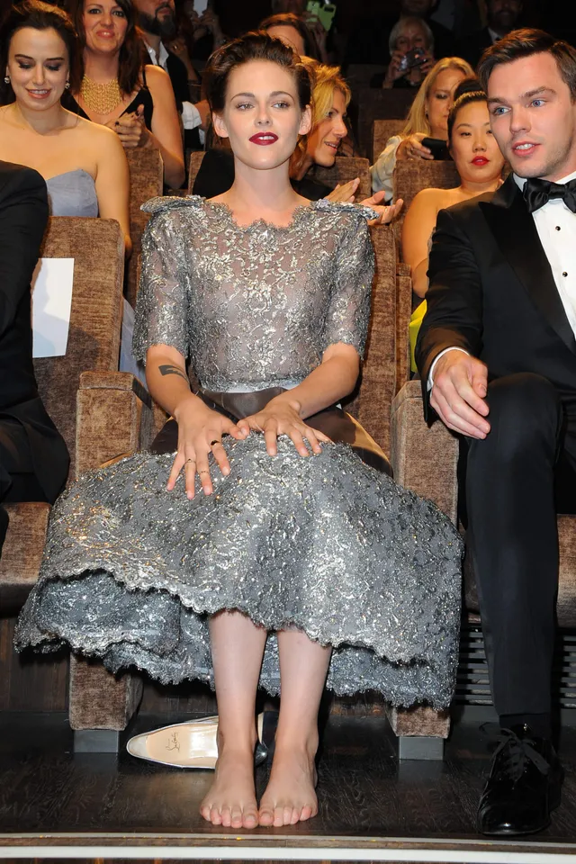 Kristen Stewart sitting barefoot in a sparkling dress at an event.