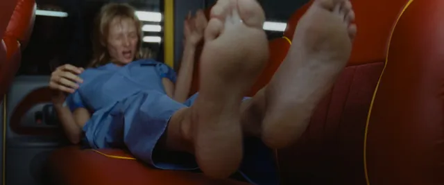 Uma Thurman reclining barefoot in a blue outfit in a film scene.