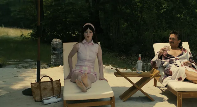 Sophie Thatcher kneeling on a sun lounger beside a man in a film scene.