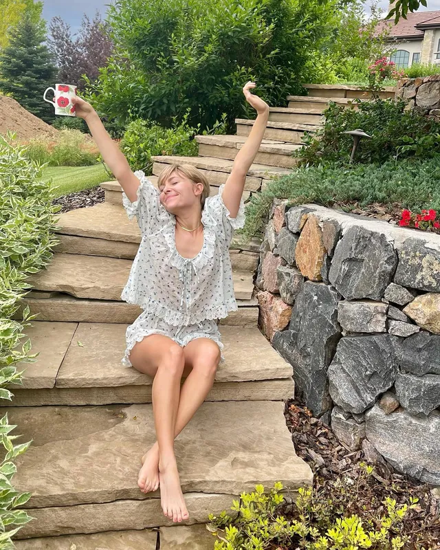 AnnaSophia Robb sitting on garden steps in a light patterned dress.