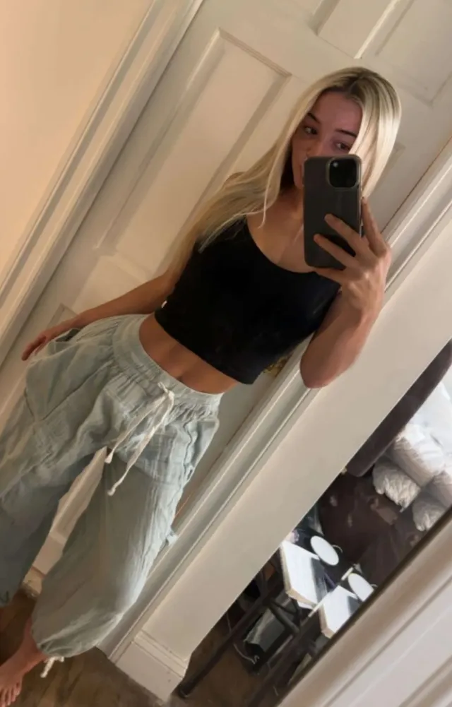 Olivia Dunne taking a mirror photo in a black top and pale trousers.